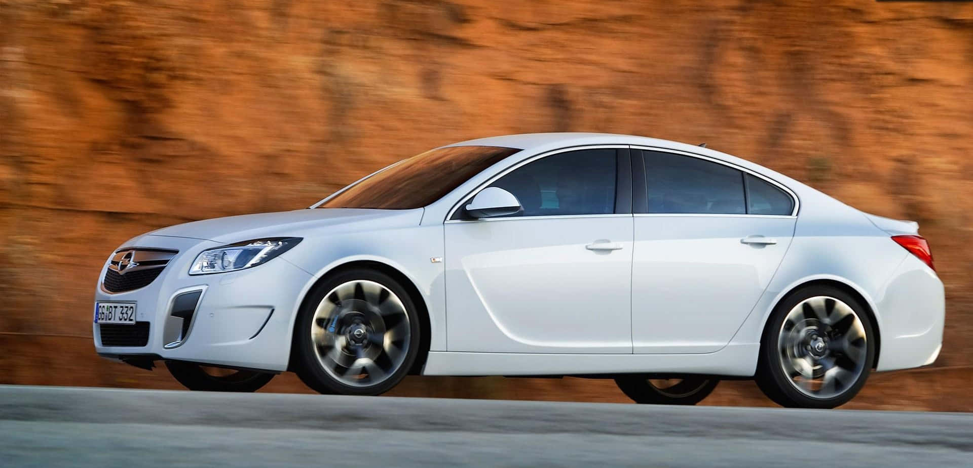 Opel Insignia 桌布 壁紙 — 一輛時尚的白色轎車在道路上疾馳，背景是模糊的橙色懸崖。
