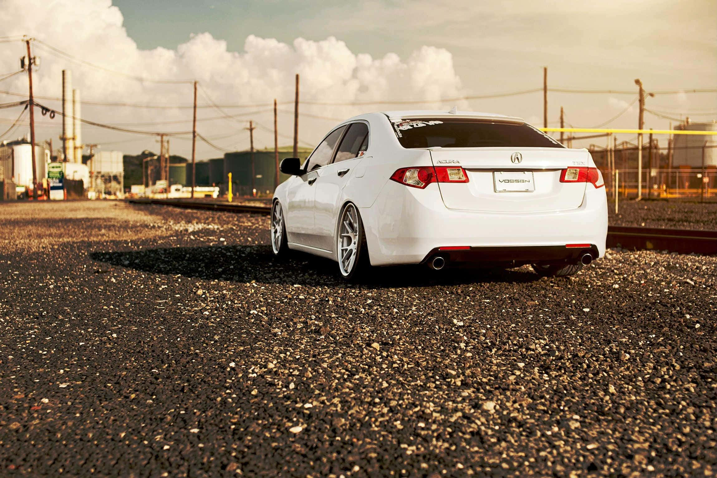 Acura Tsx 桌布 壁紙 — 一輛時尚的白色跑車停放在工業區附近的碎石地上，天空多雲。