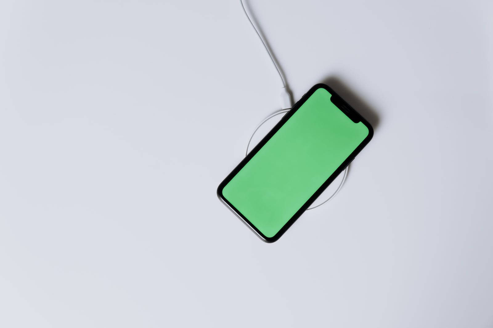 智慧型手機在白色背景上以綠色螢幕充電 — iPhone X 壁紙