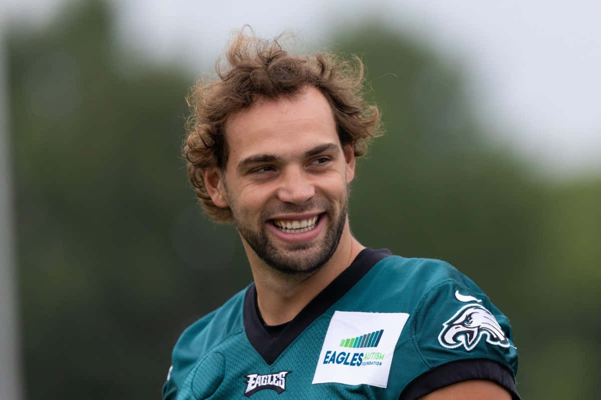  壁紙 — 一位微笑的足球員身穿藍綠色Eagles球衣，帶有自閉症意識臂章，站在戶外，背景是模糊的綠色。