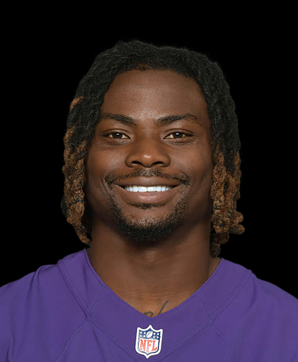  壁紙 — 一位面帶微笑、辮子頭髮的NFL美式足球員，在黑色背景前穿著紫色球衣。
