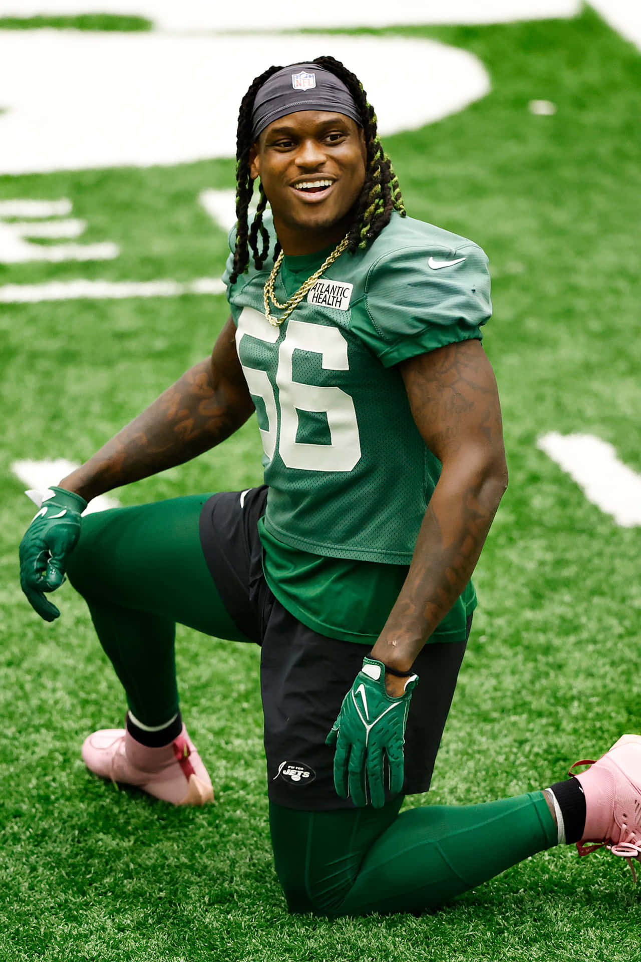  壁紙 — 一位微笑的NFL球員身穿綠色56號球衣，在充滿活力的足球場上跪著，腳穿粉紅色釘鞋。