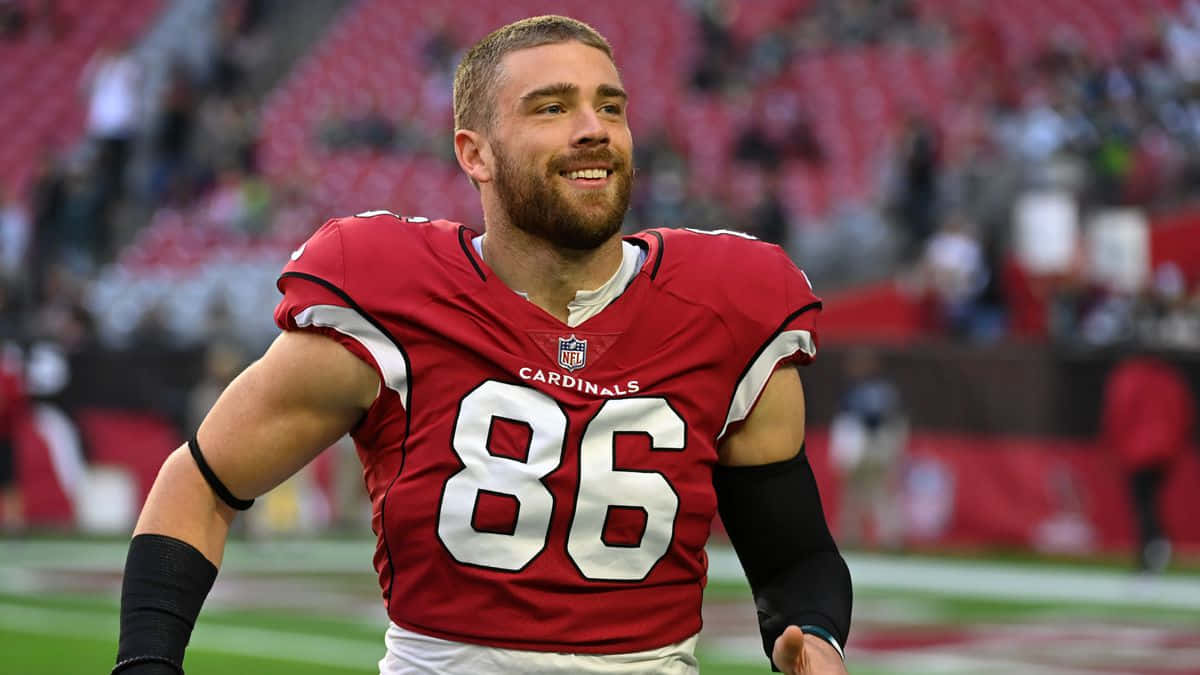  壁紙 — 一位微笑的NFL外接手身穿紅色紅雀隊86號球衣，在綠色球場上奔跑，身後是模糊的體育場座位。