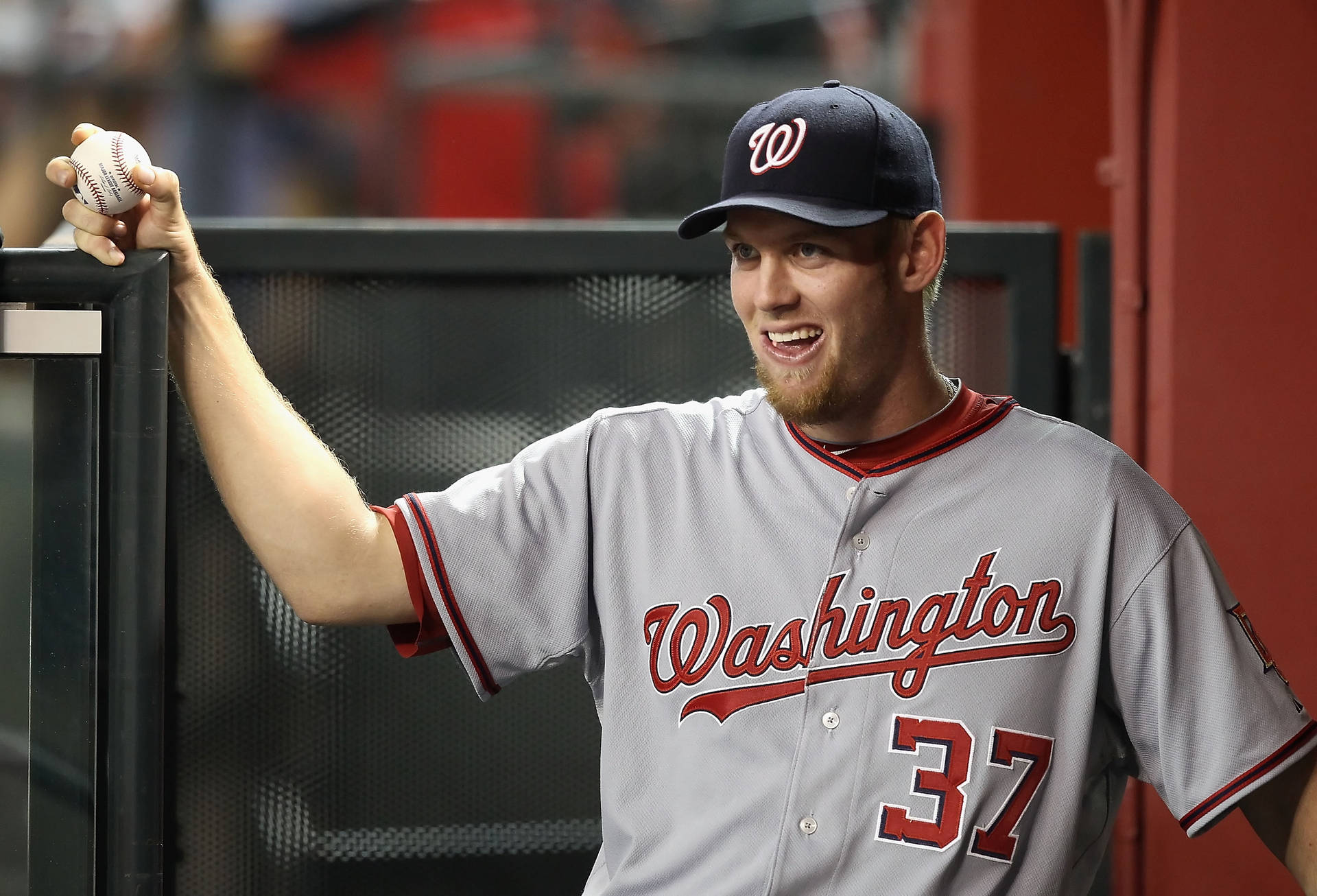 身穿華盛頓隊服的棒球運動員在休息區手持棒球微笑。 — MLB 壁紙
