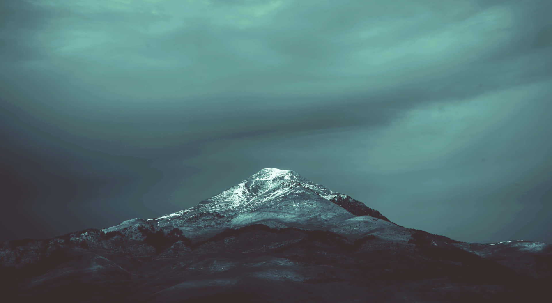  壁紙 — 白雪覆蓋的山峰在厚重的雲層下刺穿陰鬱的青灰色天空。