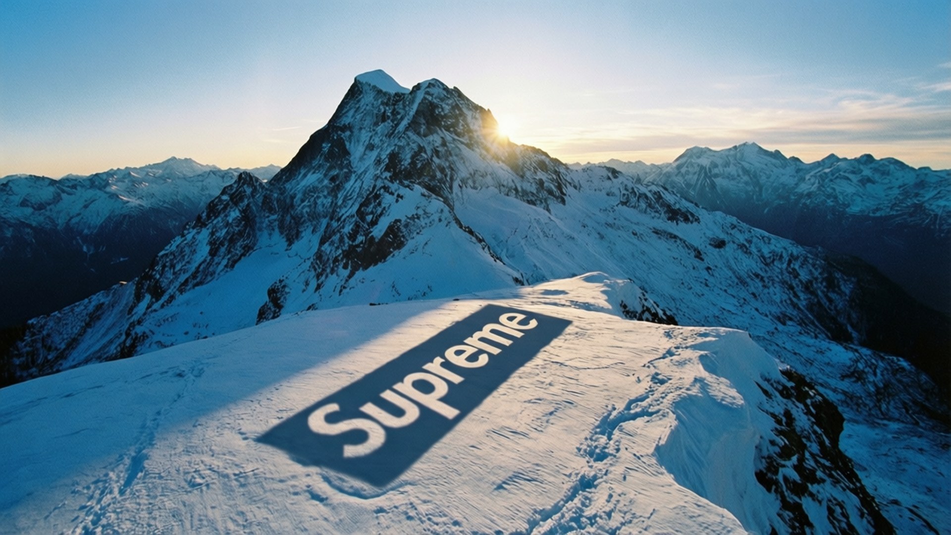 Supreme Mountain Peak 壁紙 — 日出時分，白雪覆蓋的山頂上，一個巨大的Supreme標誌嵌入雪中。