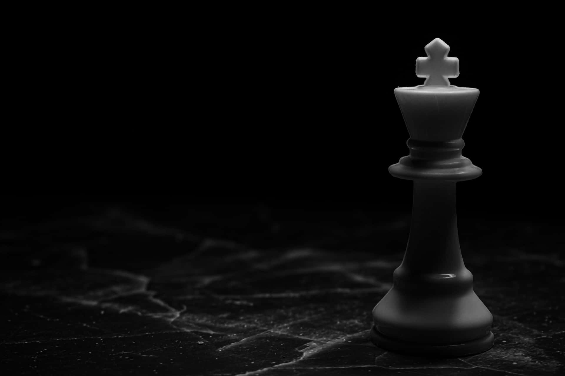  壁紙 — 一個孤獨的白色西洋棋國王在黑色大理石表面上戲劇性地照亮，呈現鮮明的單色。