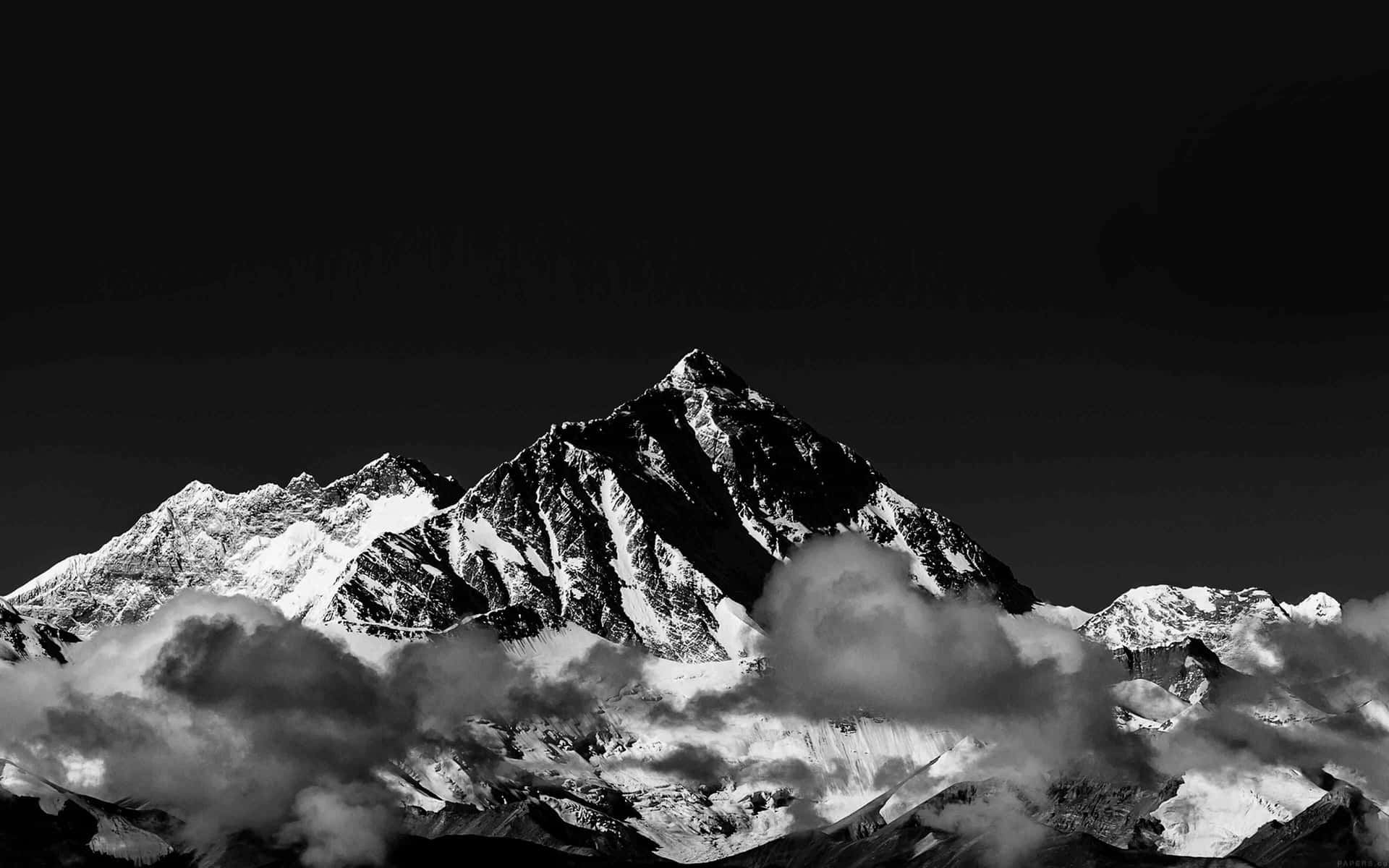  壁紙 — 一座鮮明的黑白山峰刺穿烏雲，積雪的山脊在虛空天空中閃耀。