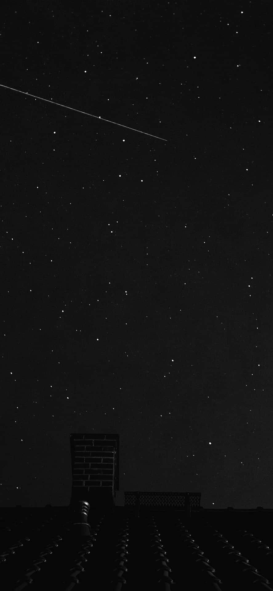 一顆流星劃過屋頂煙囪上方的繁星夜空。 — iPhone 11 Pro Max 壁紙