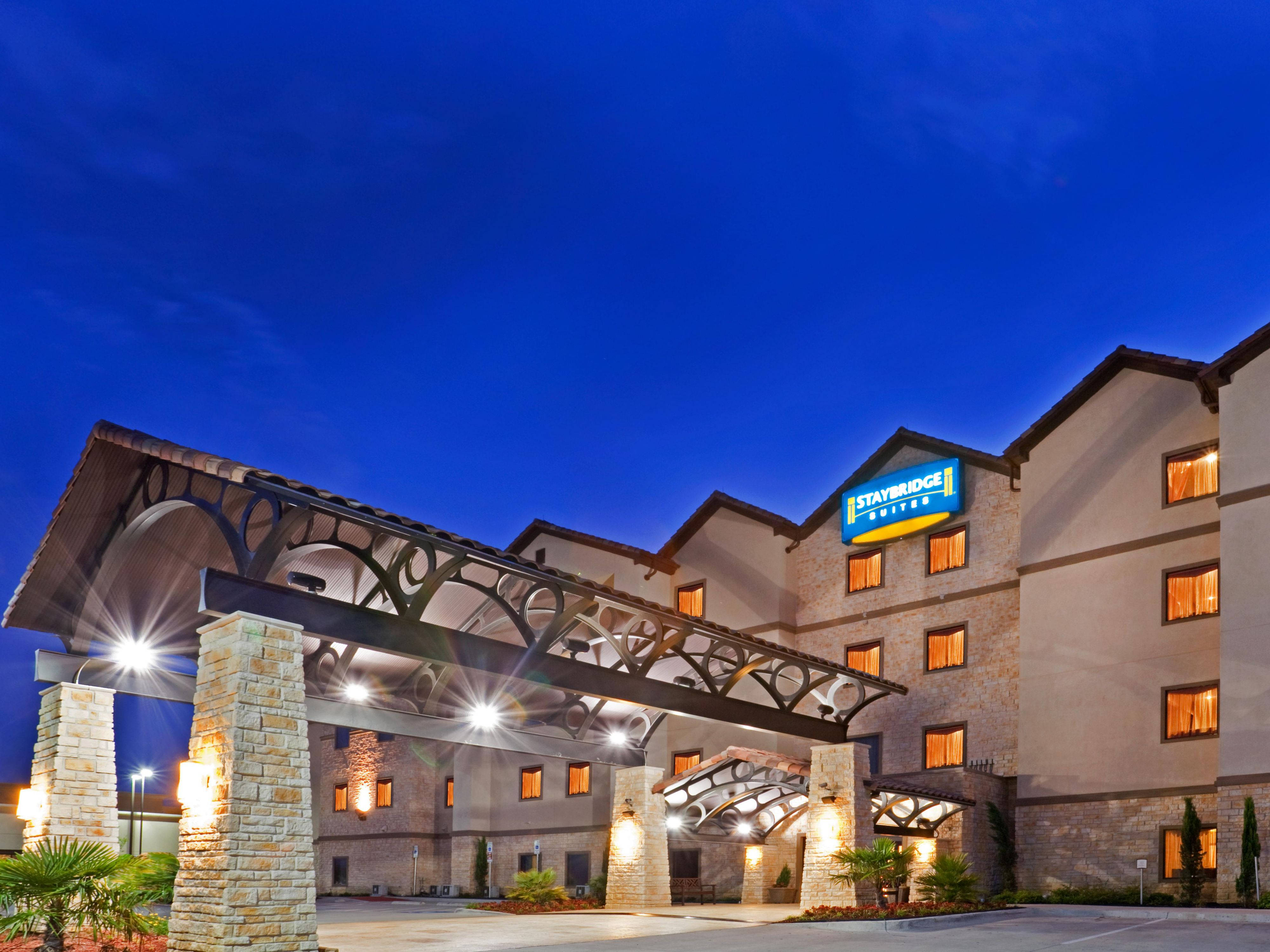 Blue Sky 桌布 壁紙 — Staybridge Suites 酒店在暮色天空下溫暖地發光，配有石拱門和明亮的窗戶。