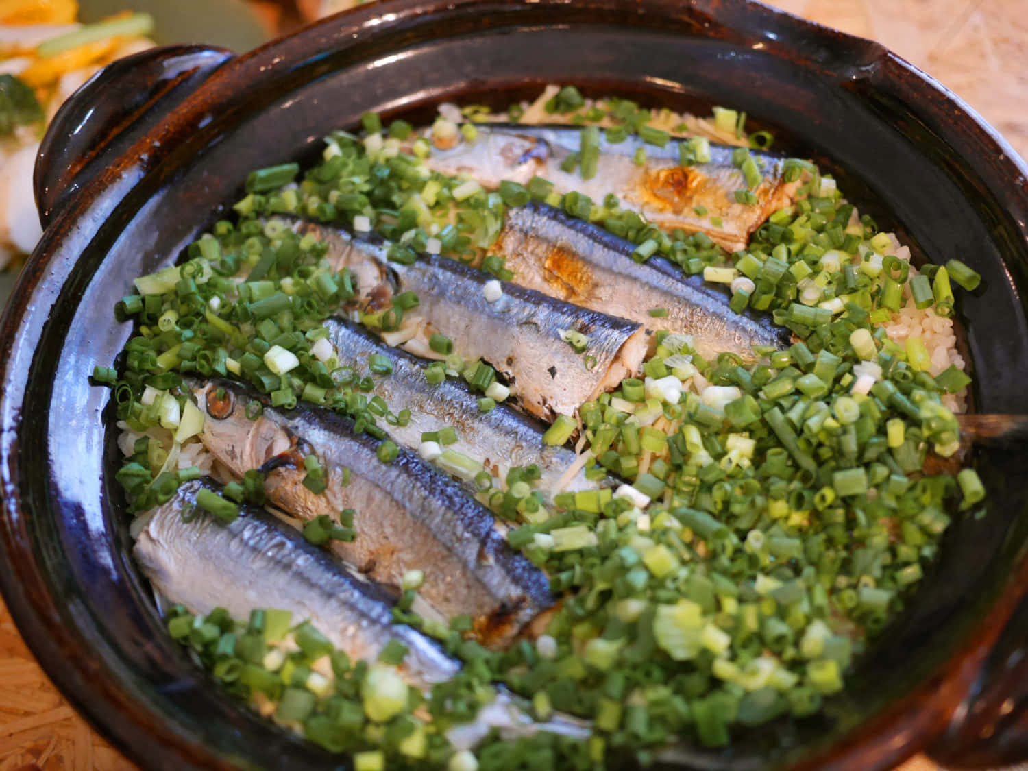  壁紙 — 一個冒著蒸氣的砂鍋，裡面裝滿了米飯，上面放著烤沙丁魚和切碎的青蔥。