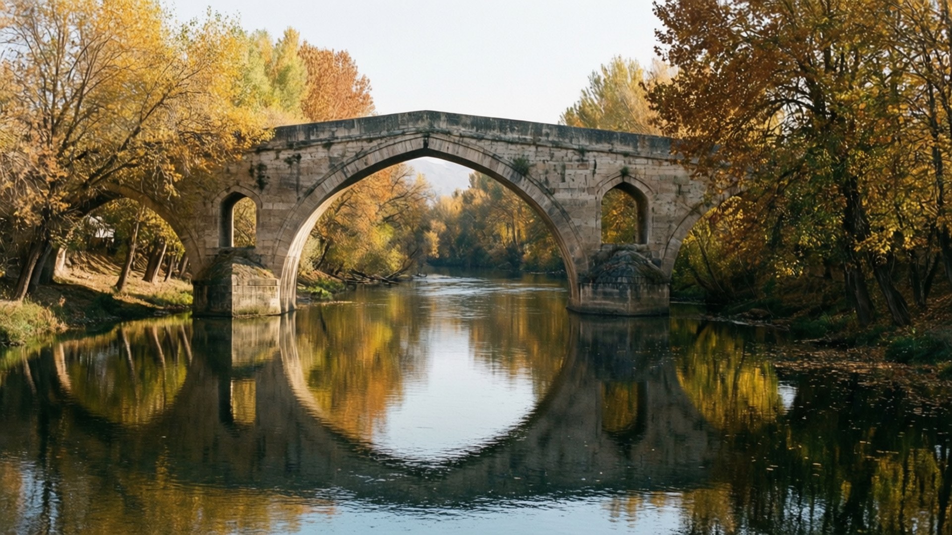 Taş Köprü Autumn 壁紙 — 一座石拱橋橫跨平靜的河流，周圍是金色的秋樹，倒映在水中。