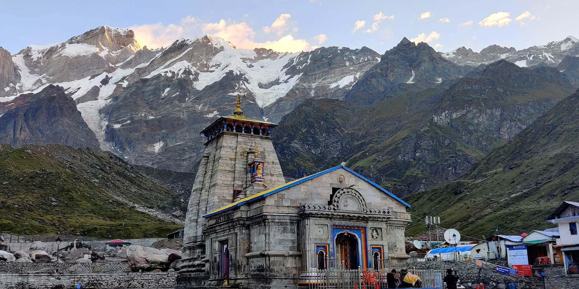 Kedarnath 桌布 壁紙 — 一座帶有色彩繽紛點綴的石廟矗立在巍峨的雪山前，背景是柔和的暮色天空。