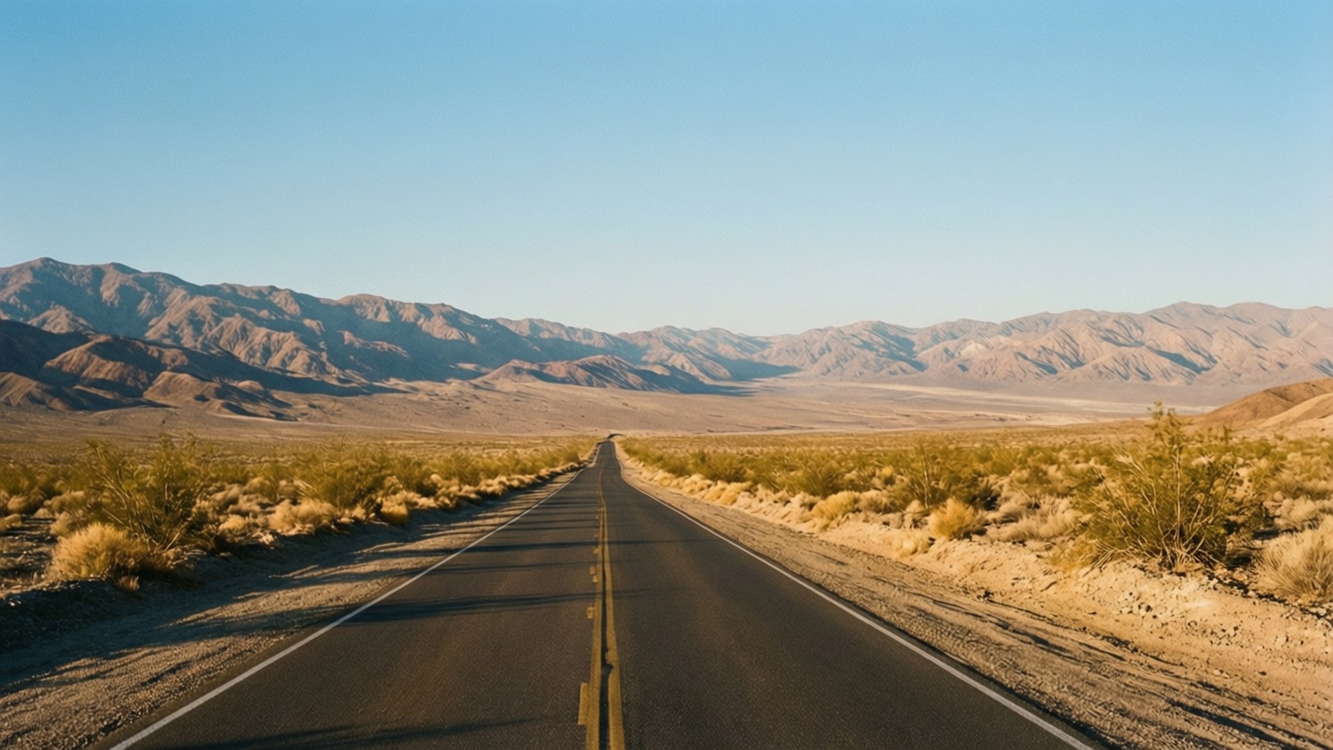 macOS Mojave 桌布 壁紙 — 一條筆直的沙漠高速公路在清澈藍天和金色光芒下延伸至遠山。