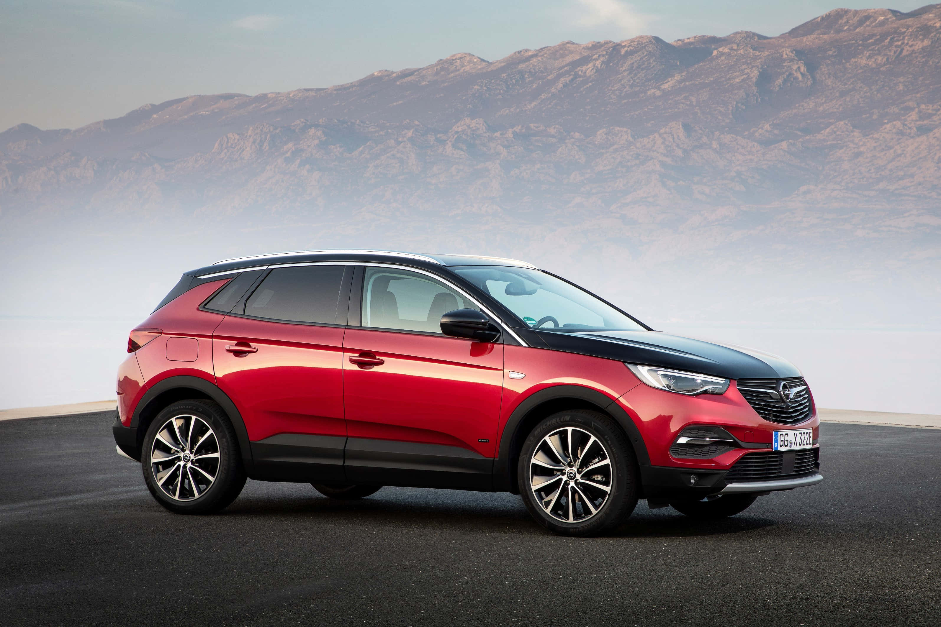 Opel Grandland X 桌布 壁紙 — 一輛引人注目的紅色和黑色歐寶SUV停在瀝青路上，背景是朦朧的崎嶇山脈。