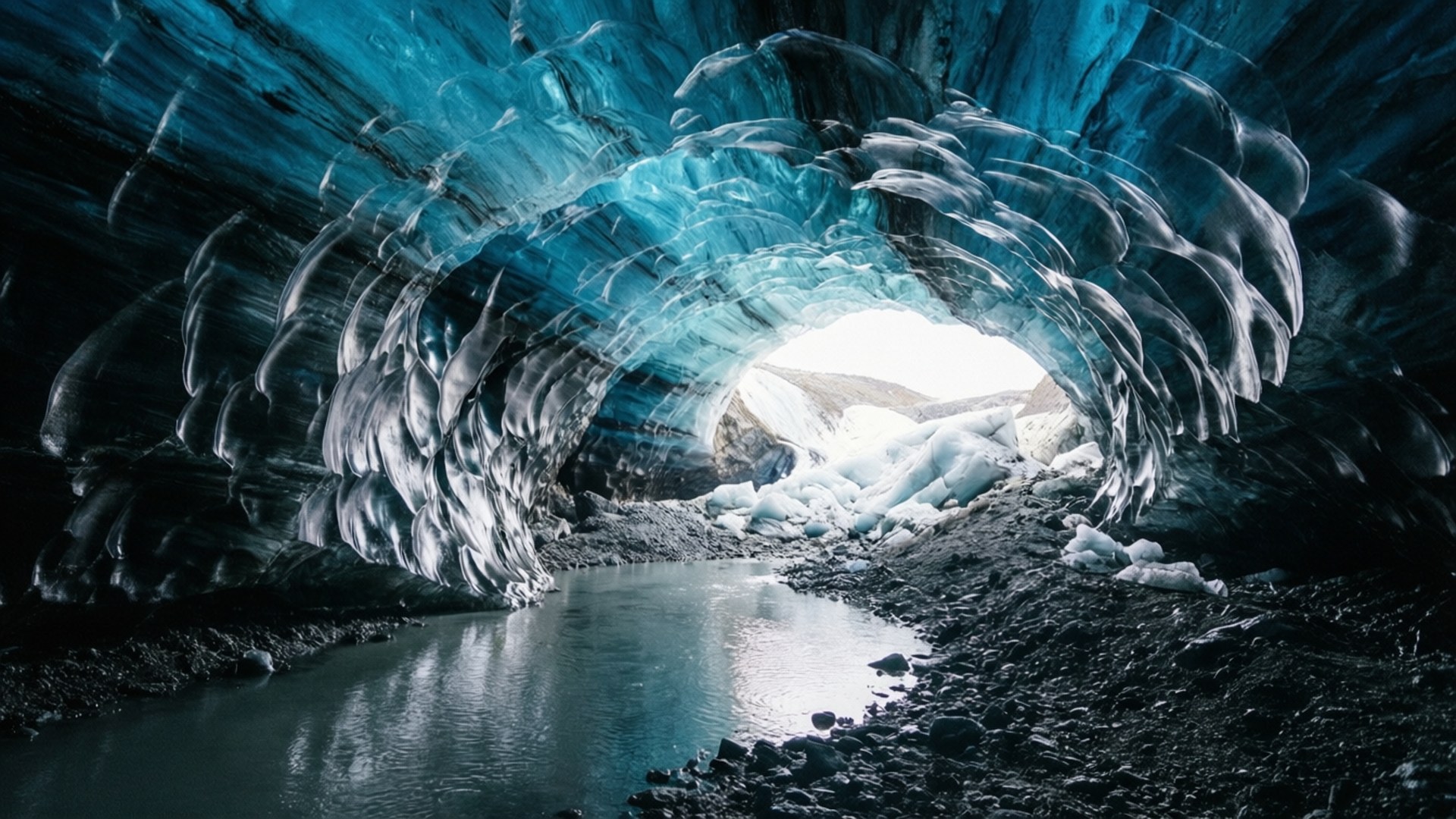 Antarctic Ice Cave Interior 壁紙 — 一個令人驚嘆的藍色冰洞，上方有水晶般的結構拱起，下方有反射池。