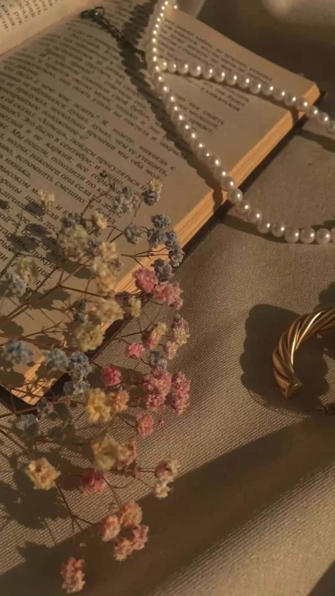  壁紙 — 一幅陽光照射的靜物畫，乾花、珍珠和金手鐲放在一本打開的書上，帶有溫暖的金色陰影。