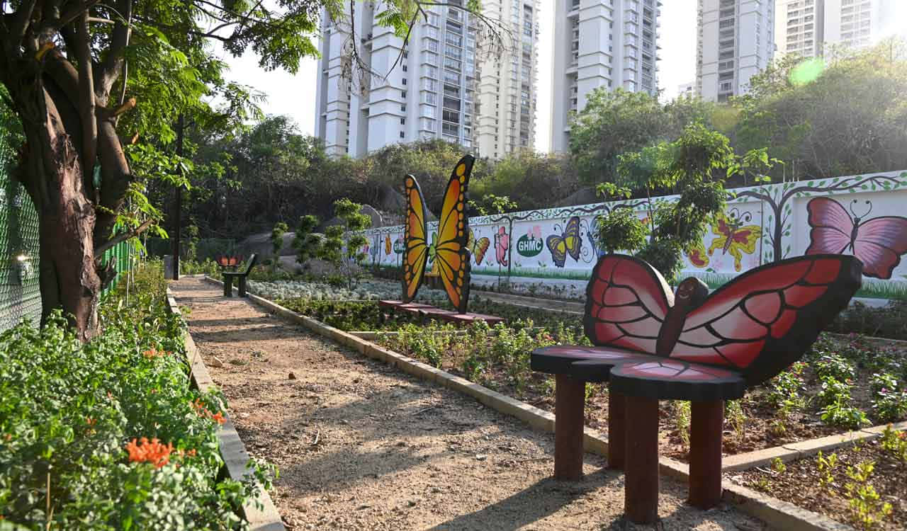  壁紙 — 一條陽光普照的城市花園小徑，兩旁擺放著蝴蝶主題的長椅和壁畫，被樹木和高聳的公寓大樓環繞。