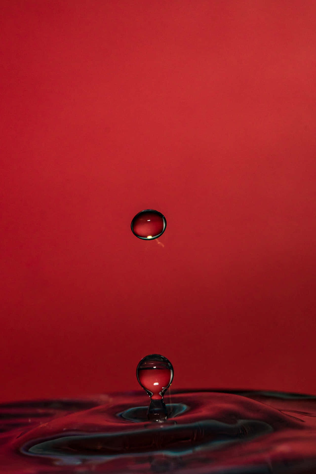 水滴懸浮在漣漪池上方，背景為紅色。 — 4K 壁紙
