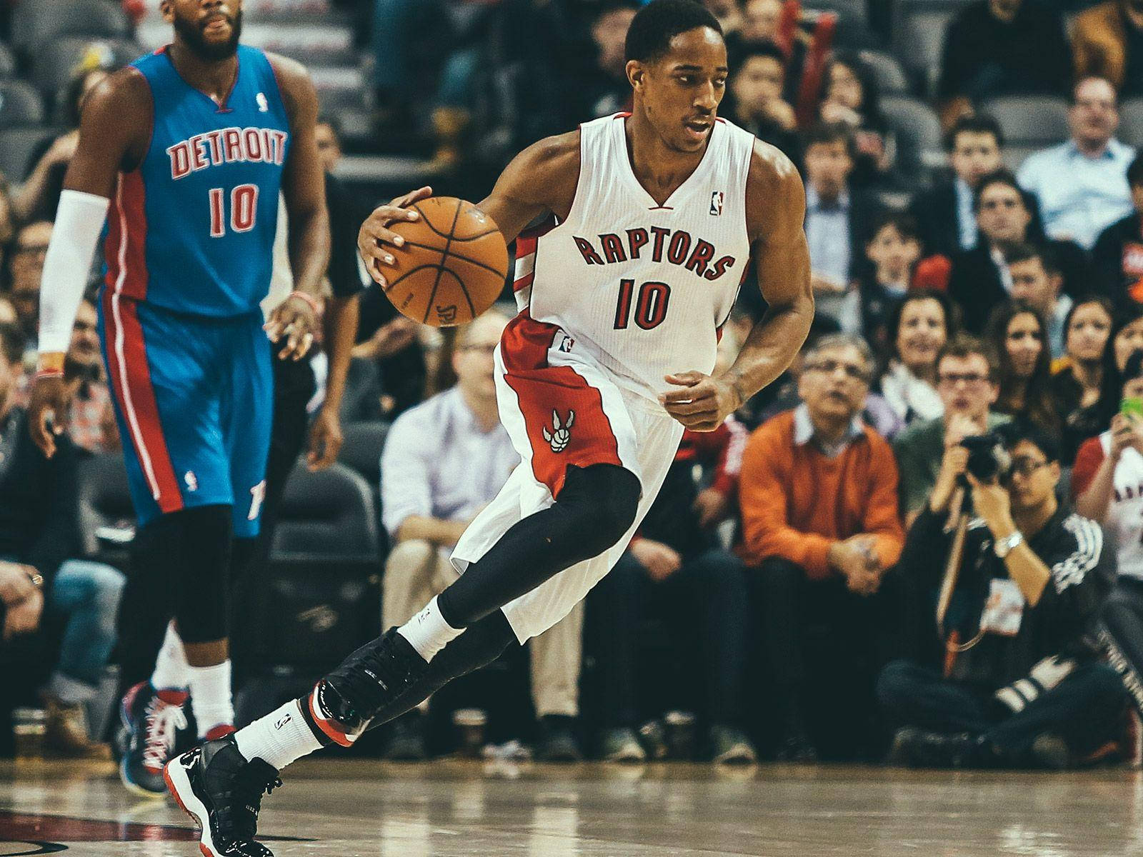 多倫多暴龍隊籃球球員在比賽中運球，背景有觀眾。 — NBA 壁紙