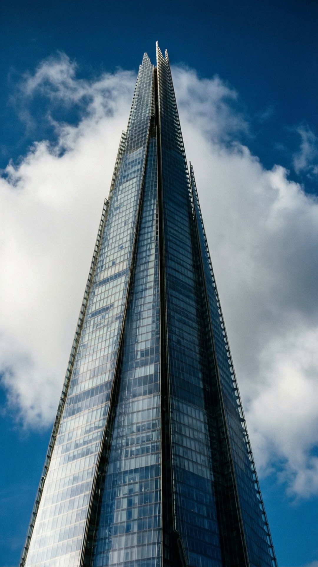 The Shard Skyscraper 壁紙 — 一座高聳的玻璃摩天大樓，帶有尖銳的尖頂，刺破點綴著蓬鬆白雲的鮮豔藍天。
