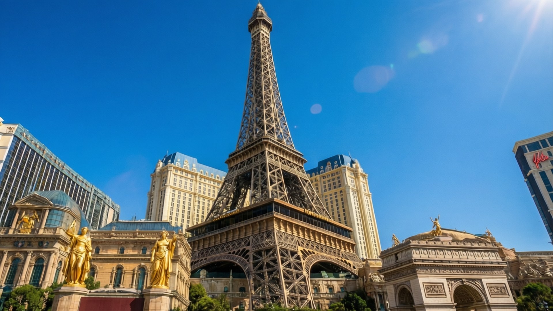 Paris Las Vegas Day 壁紙 — 一座高聳的艾菲爾鐵塔複製品矗立在燦爛的藍天下，金色雕像矗立在其兩側，豪華酒店在後方升起。