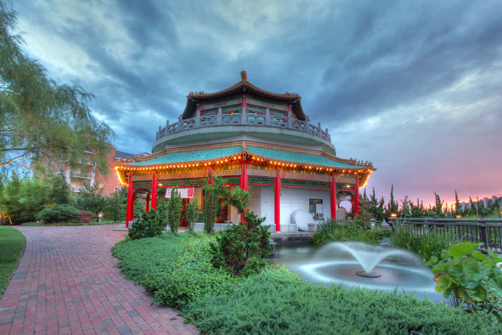 暮色中發光的中式亭閣，在園林花園中設有噴泉和磚砌小徑。 — 台灣 壁紙