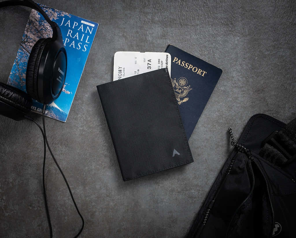  壁紙 — 一個旅行裝備組合，包括護照、鐵路通行證、耳機和錢包，放在有紋理的灰色表面上。