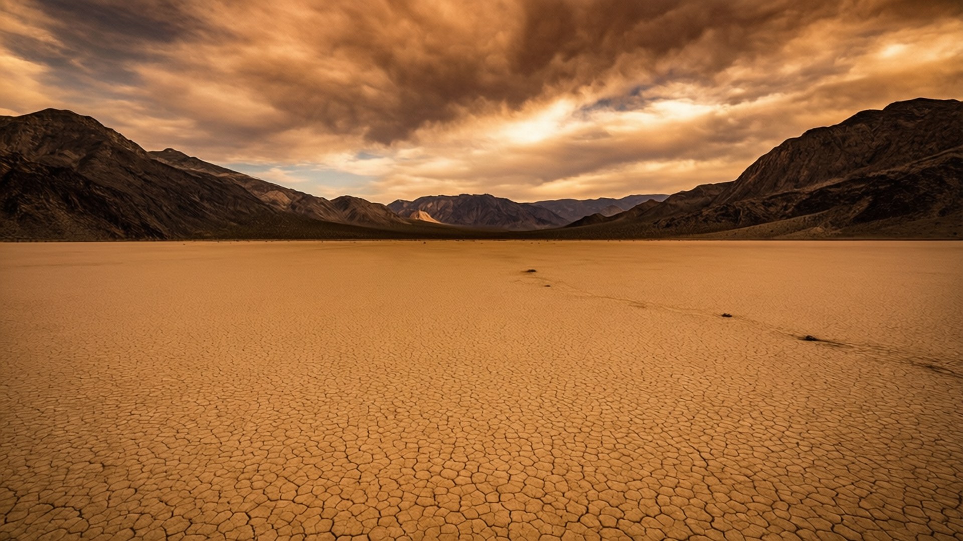 macOS Mojave Cracked Earth 壁紙 — 廣闊的龜裂沙漠地面在戲劇性的金色天空下延伸，遠方有巍峨的山脈。