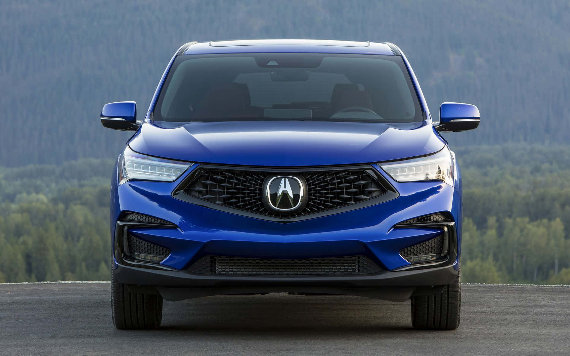 Acura Rdx 桌布 壁紙 — 一輛充滿活力的藍色Acura SUV在鋪砌的道路上向前行駛，背景是晴朗日光下的森林山脈。