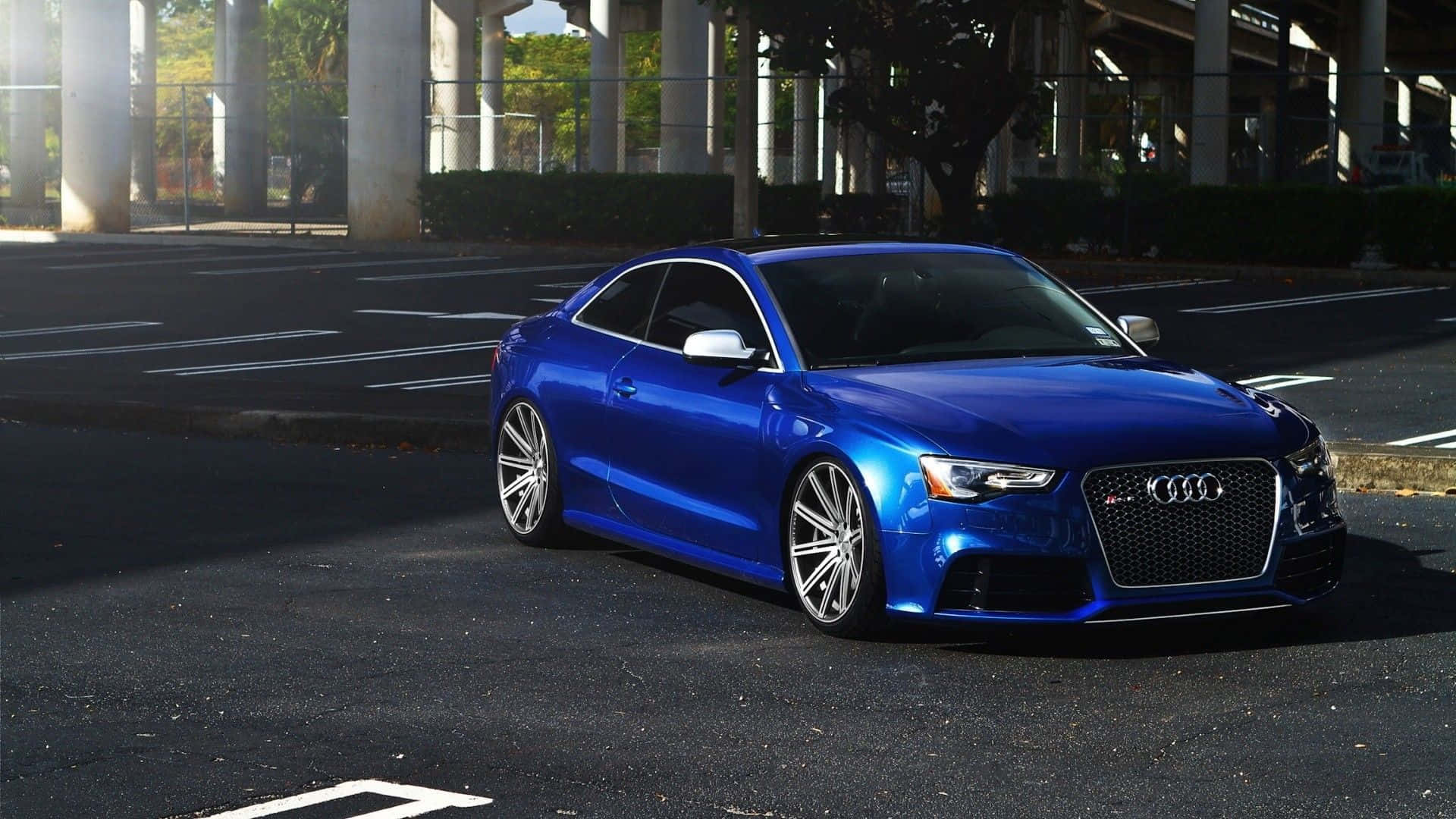 Audi S6 桌布 壁紙 — 一輛充滿活力的藍色奧迪RS3雙門跑車停在天橋下，陽光突顯其流暢線條和定制輪圈。