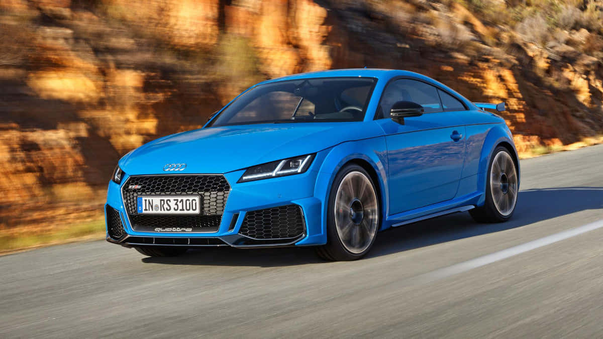 Audi Tt Rs 桌布 壁紙 — 一輛充滿活力的藍色奧迪TT RS在蜿蜒的道路上飛馳，背景是模糊的橙色岩石懸崖。