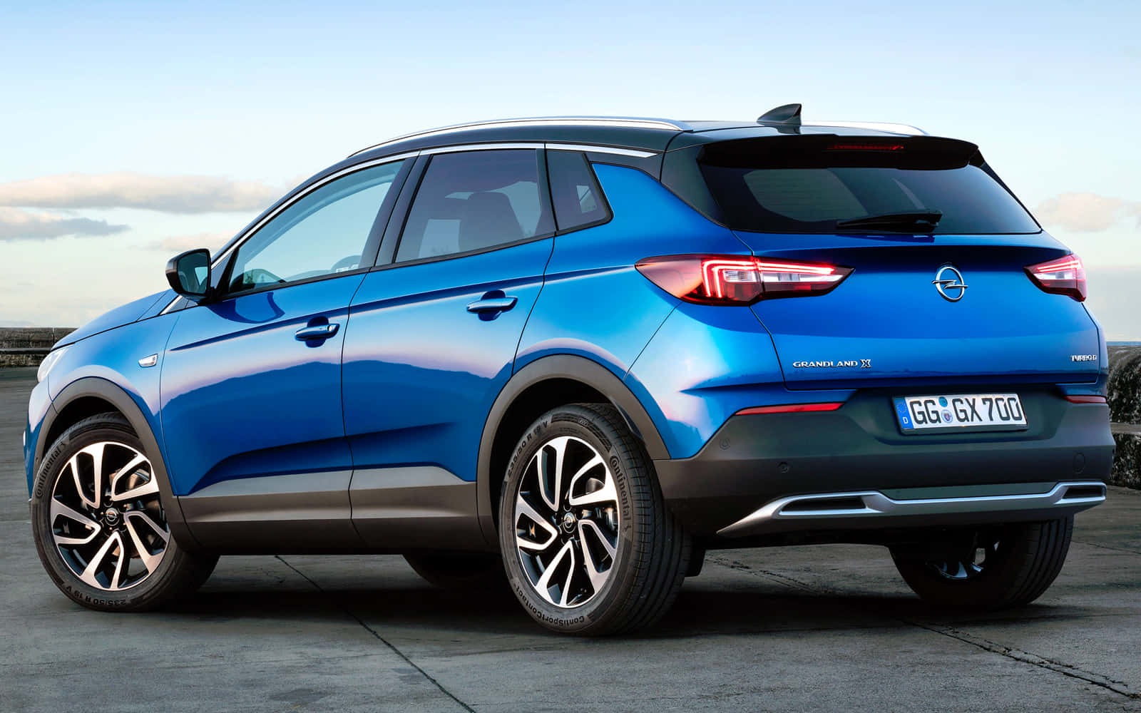 Opel Grandland X 桌布 壁紙 — 一輛鮮藍色的Opel Grandland X SUV停泊在混凝土表面上，天空清澈，有柔軟的雲朵。