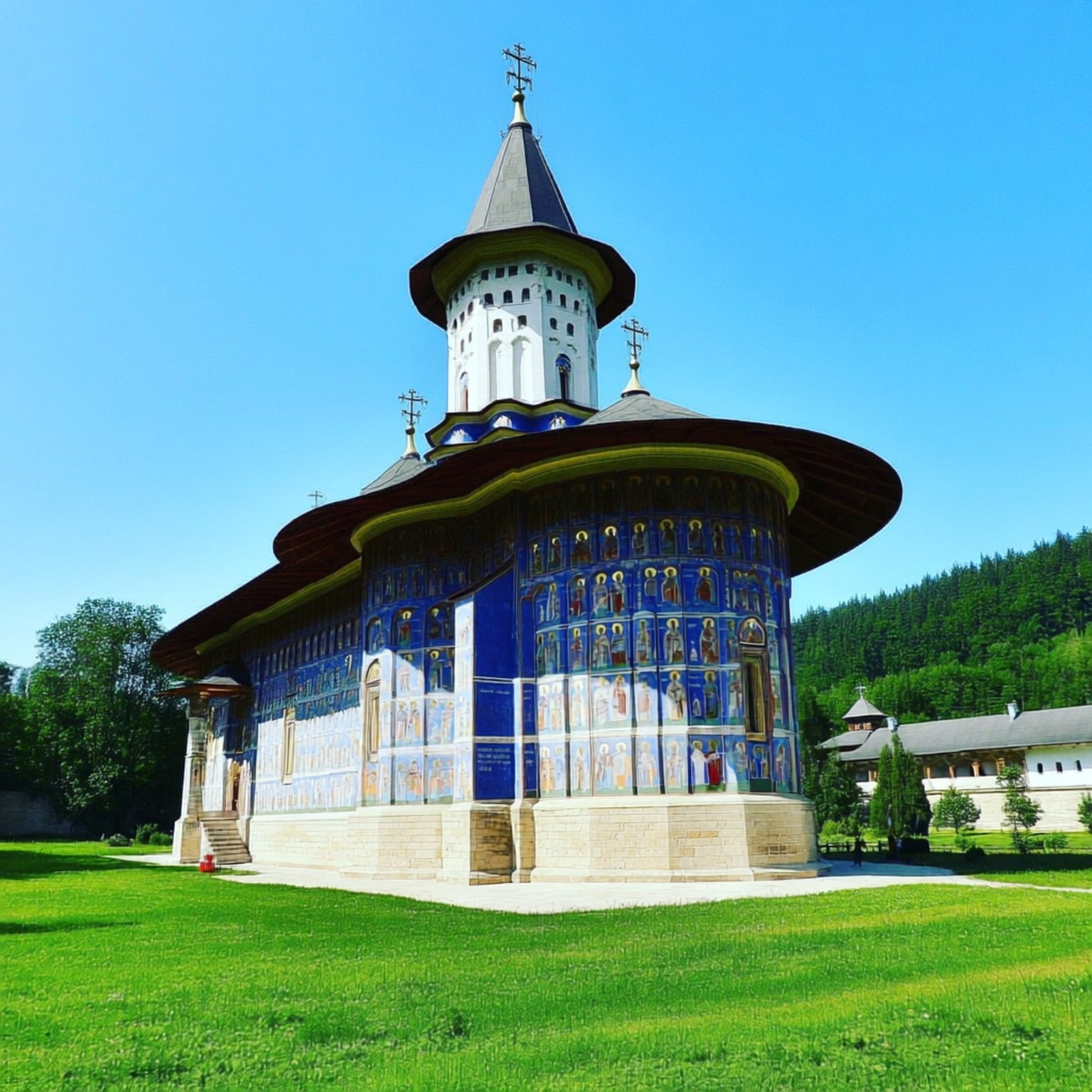 Voronet Monastery Blue 壁紙 — 一座充滿活力的藍色東正教教堂，帶有複雜的宗教壁畫，矗立在茂密的綠色草坪上，天空清澈湛藍。