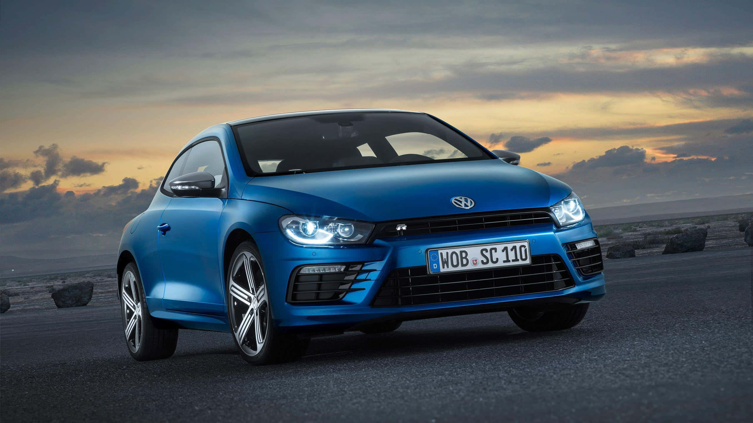 Volkswagen Scirocco 桌布 壁紙 — 一輛充滿活力的藍色福斯Scirocco跑車在戲劇性的日落天空下，在開闊的道路上閃閃發光。