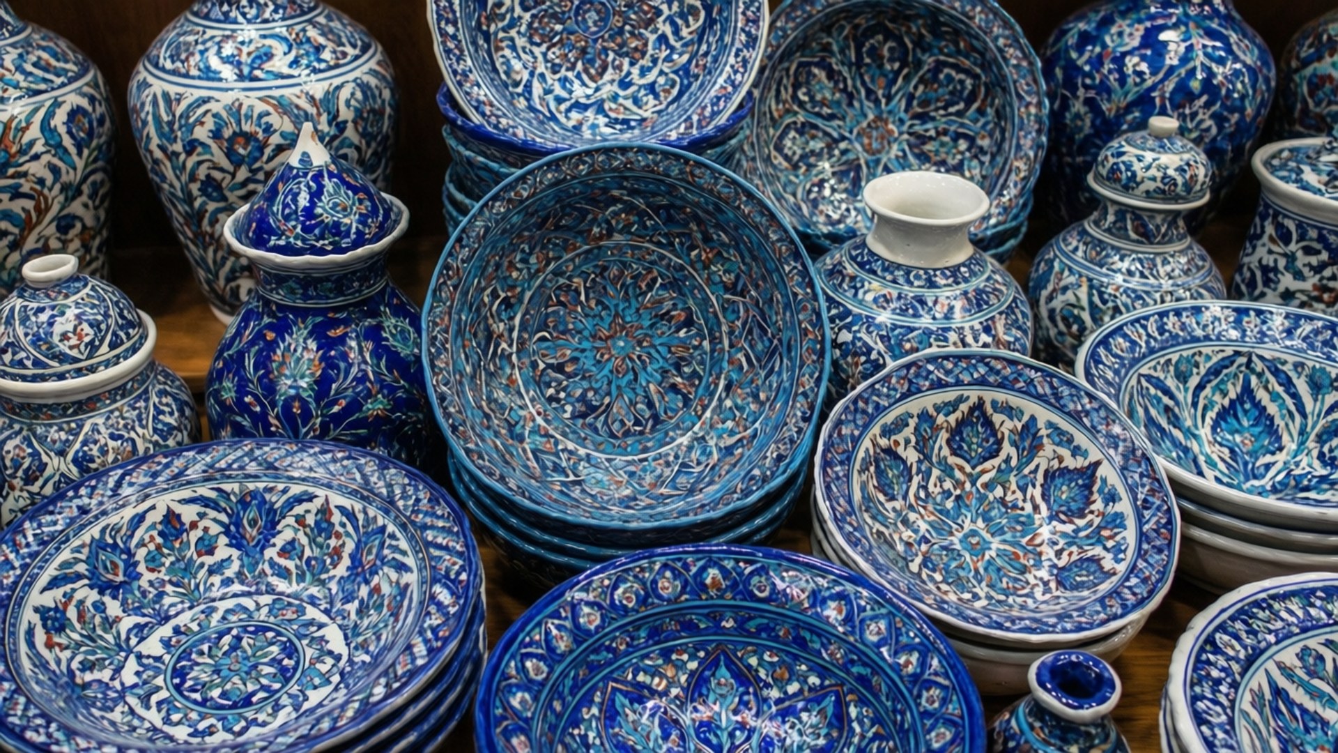 Iznik Ceramics Gallery 壁紙 — 一系列充滿活力的藍白陶瓷碗、花瓶和罐子，帶有複雜圖案，緊密排列在木質表面上。