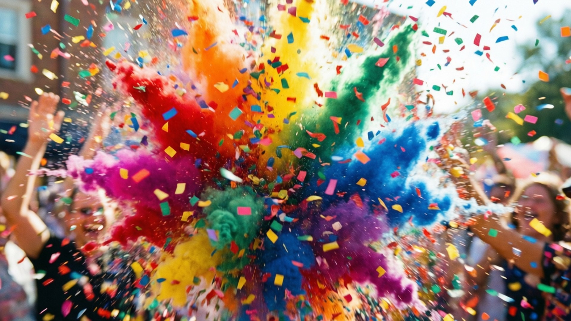 Rainbow Confetti Burst 壁紙 — 彩虹色粉末和五彩紙屑的鮮豔爆炸向外爆發，背景中的人們歡樂地慶祝。