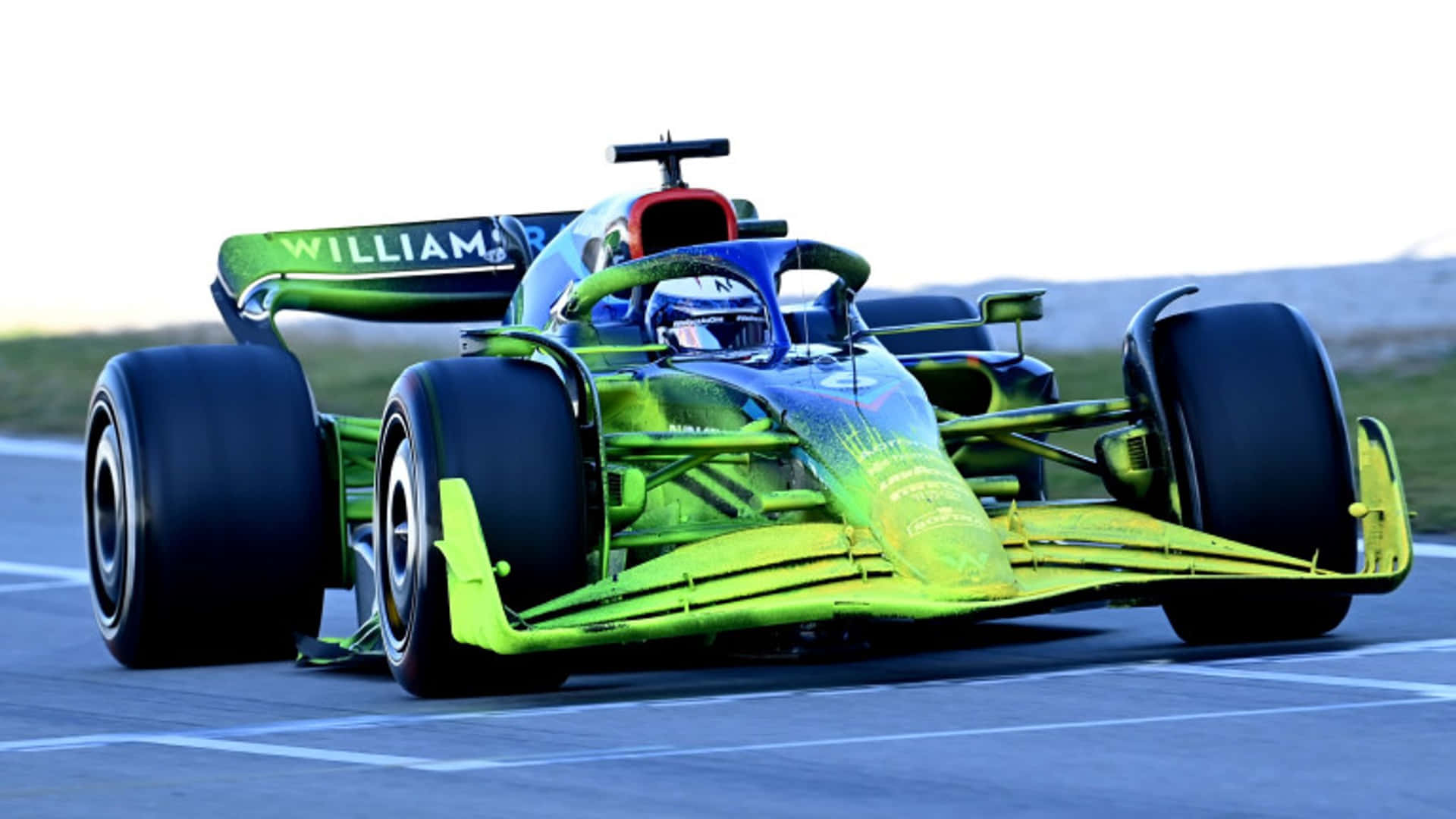 一輛綠色和藍色的一級方程式賽車在賽道上飛馳。 — F1 壁紙