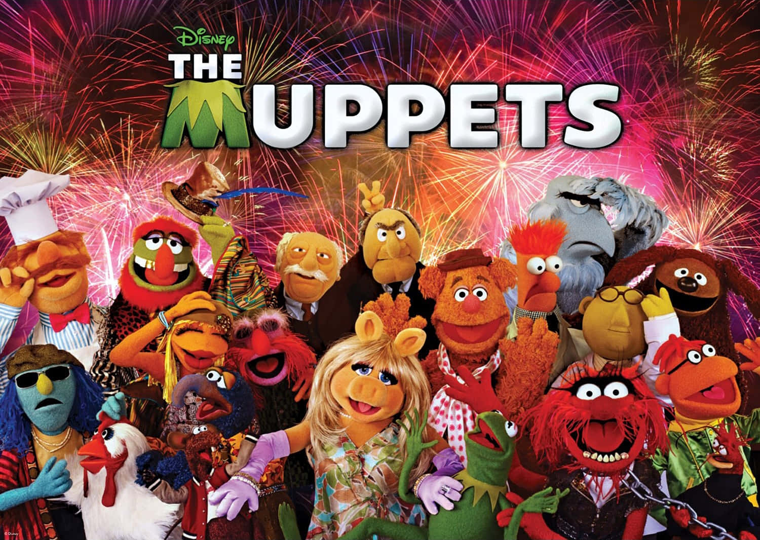  壁紙 — 一群充滿活力的Muppets角色在耀眼的紅色和金色煙火下慶祝，上方顯示標題'The Muppets'。