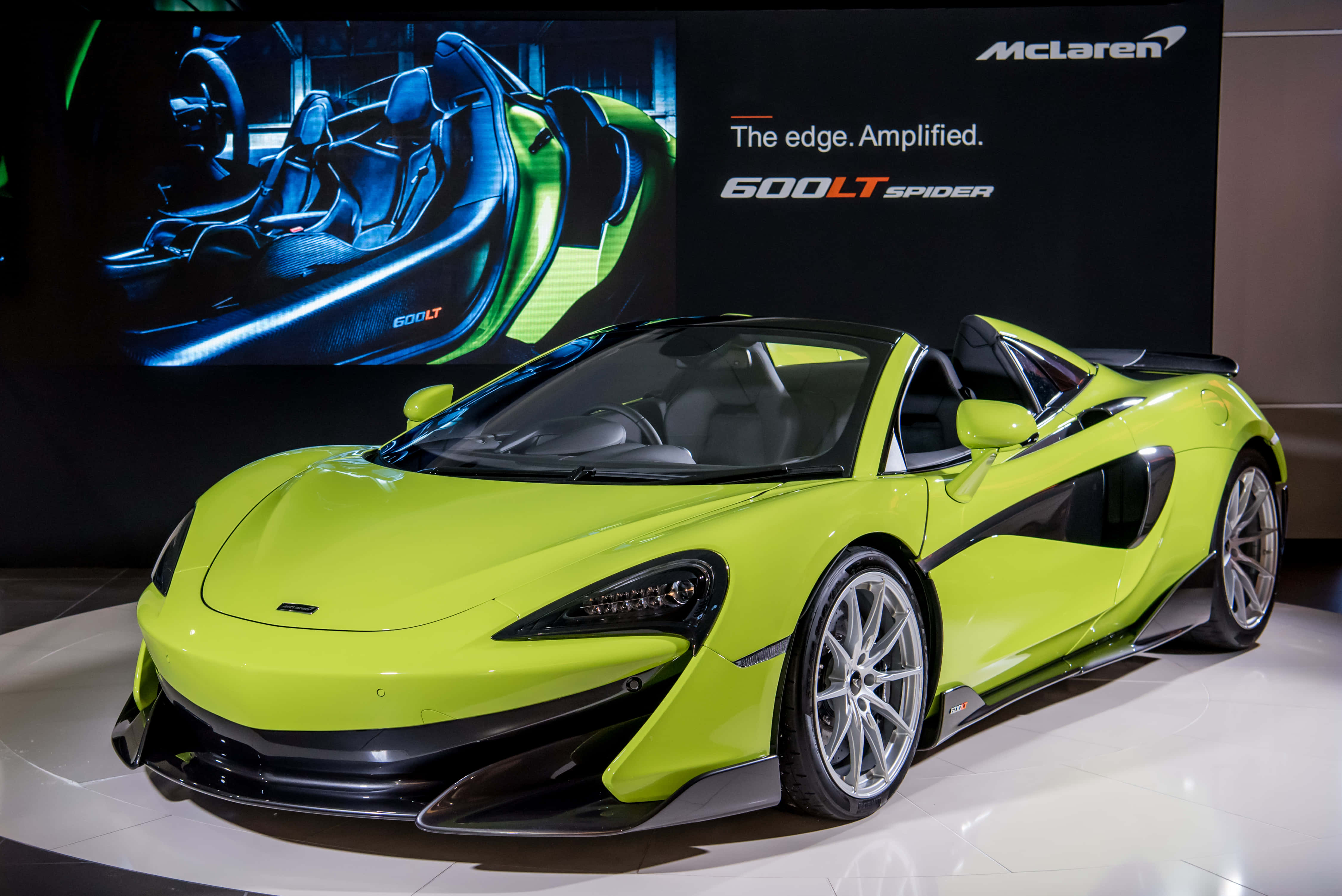 Mclaren 600lt Spider 桌布 壁紙 — 一輛充滿活力的萊姆綠色McLaren 600LT Spider跑車在車展上，在明亮的燈光下閃閃發光，背景帶有品牌標誌。
