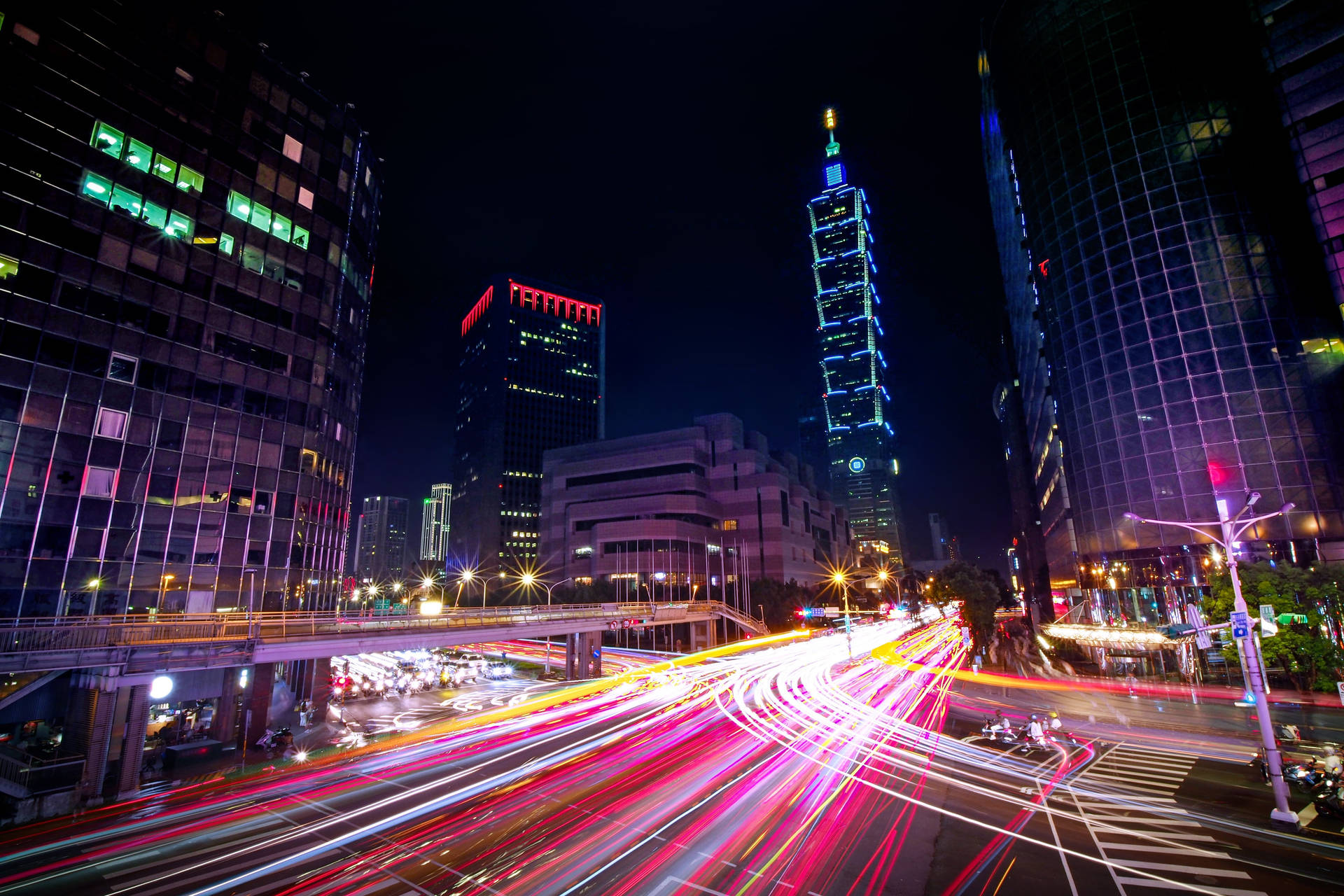 夜晚的城市街道，有移動車輛的光跡和發光的摩天大樓。 — 台灣 壁紙