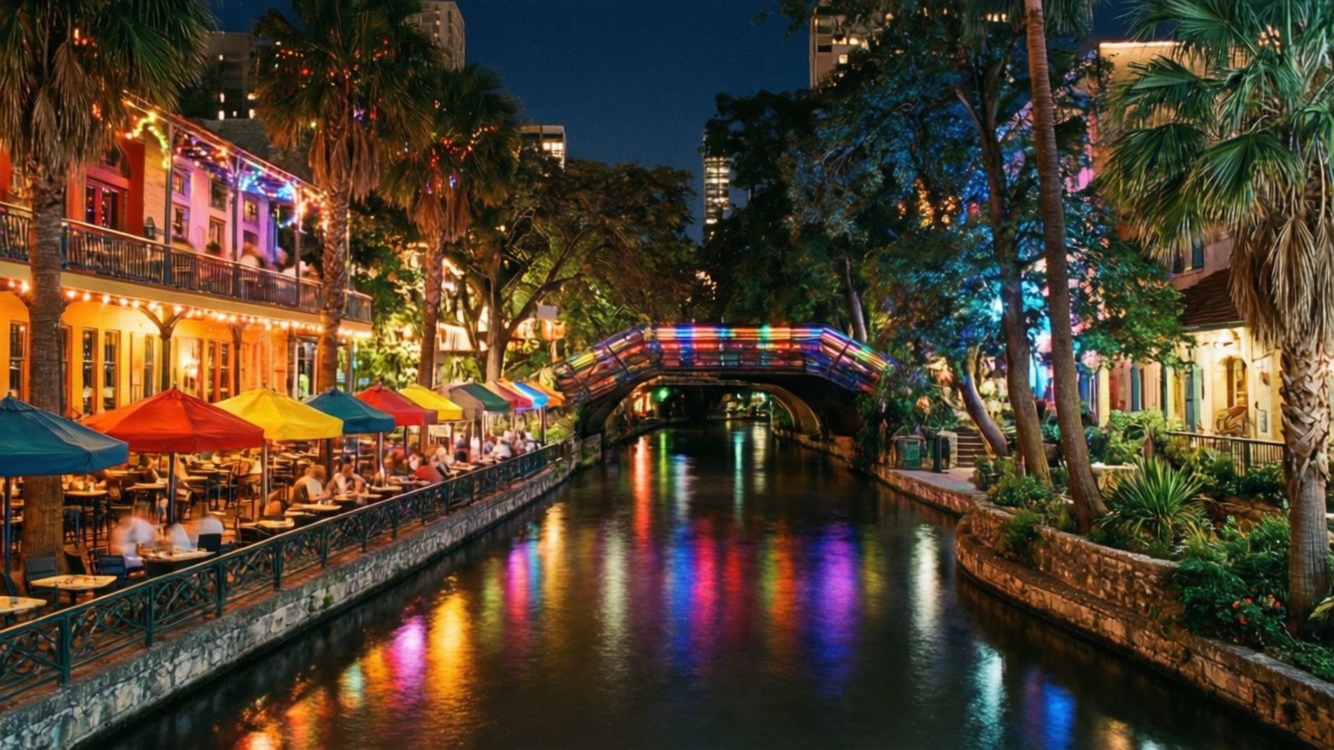 San Antonio Riverwalk Night 壁紙 — 運河旁的熱鬧夜景，彩虹燈橋倒映在水中，顧客在彩色雨傘下用餐。