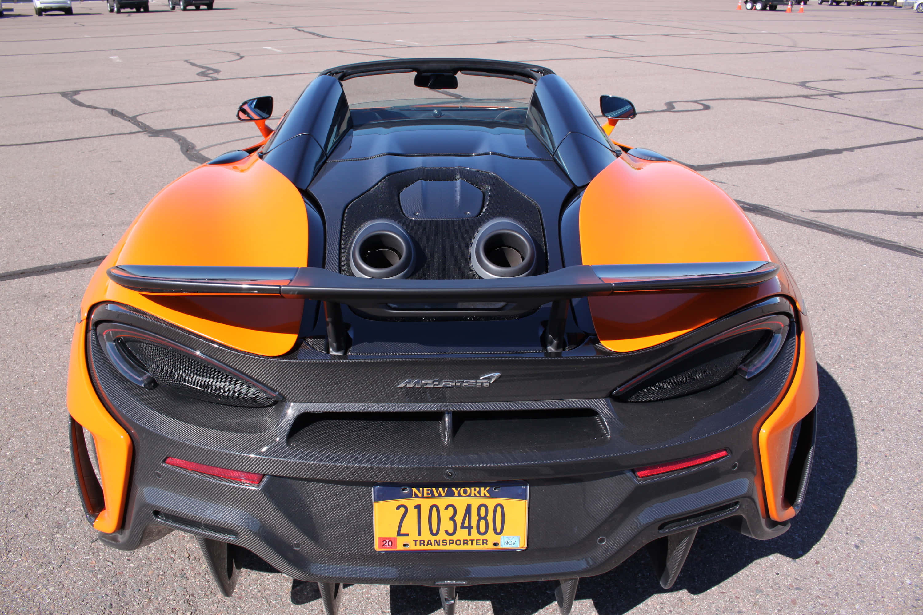 Mclaren 600lt Spider 桌布 壁紙 — 從後方觀看一輛充滿活力的橙色和黑色McLaren 600LT Spider，停在陽光明媚的瀝青場地上。