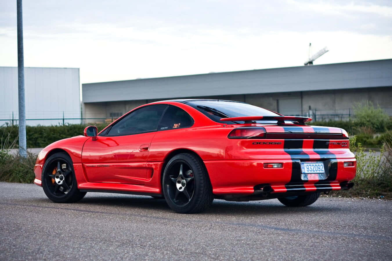 1991 Dodge Stealth 桌布 壁紙 — 一輛鮮紅色的Dodge Viper跑車，帶有黑色和藍色賽車條紋，停泊在工業建築附近的瀝青路上。