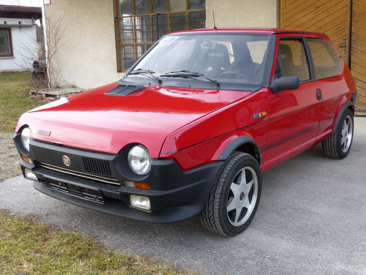 Fiat Ritmo 桌布 壁紙 — 一輛鮮紅色的菲亞特126p掀背車停在混凝土車道上，旁邊是木製車庫門。