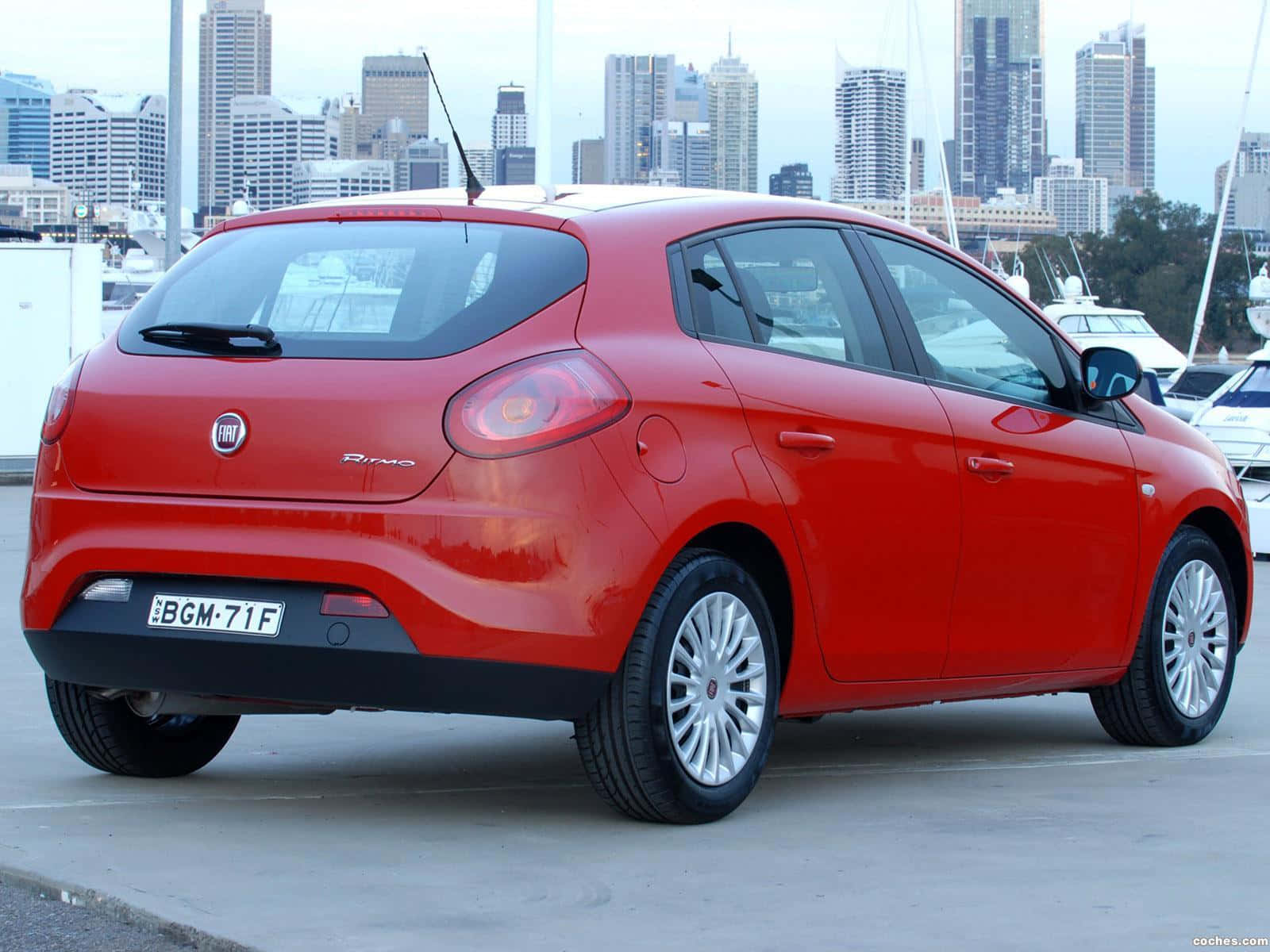 Fiat Ritmo 桌布 壁紙 — 一輛鮮紅色的飛雅特Punto停泊在海濱，背景是城市天際線。