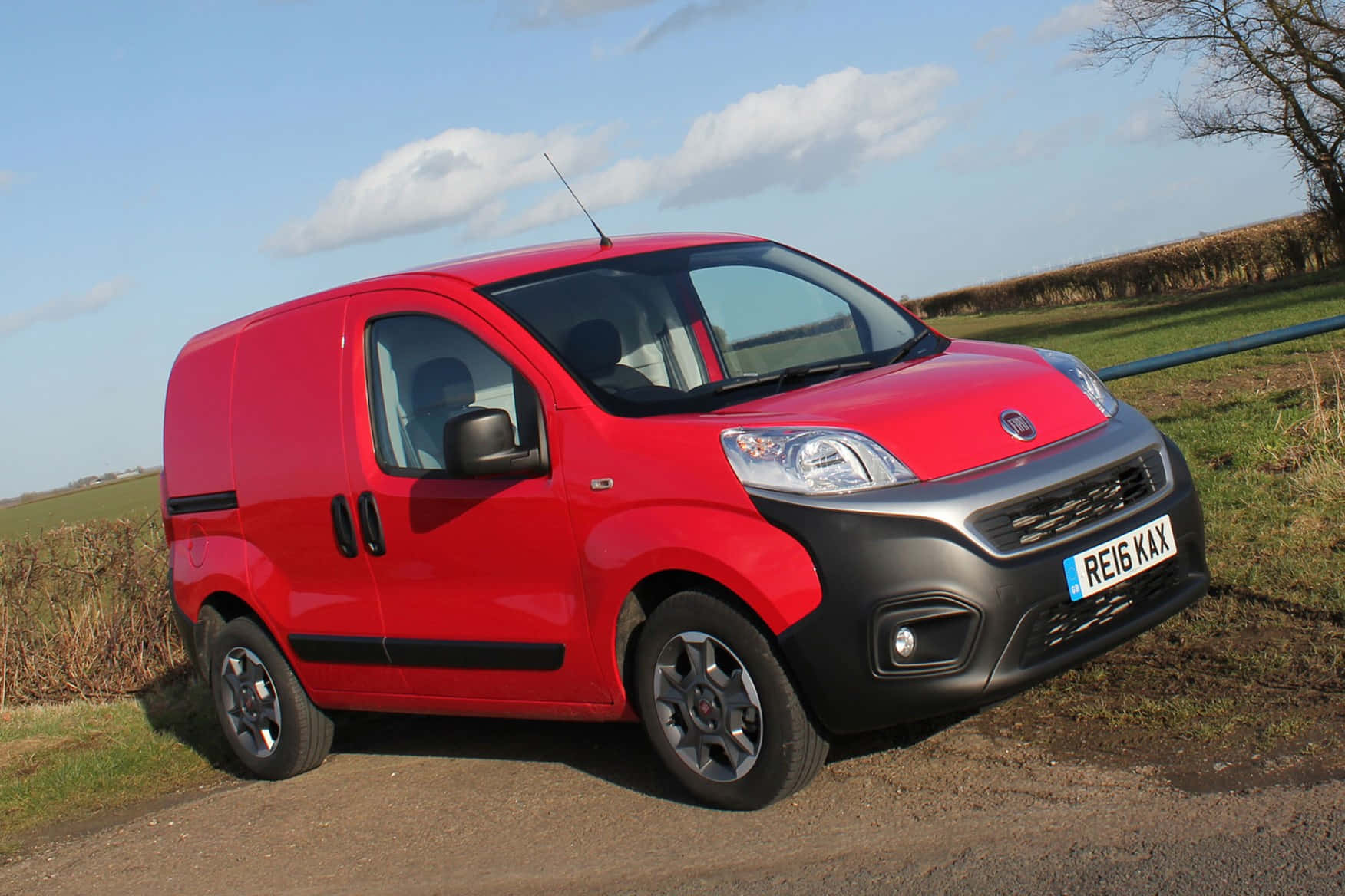 Fiat Fiorino 桌布 壁紙 — 一輛鮮紅色的Fiat廂型車停泊在碎石路上，旁邊是草地，天空局部多雲。