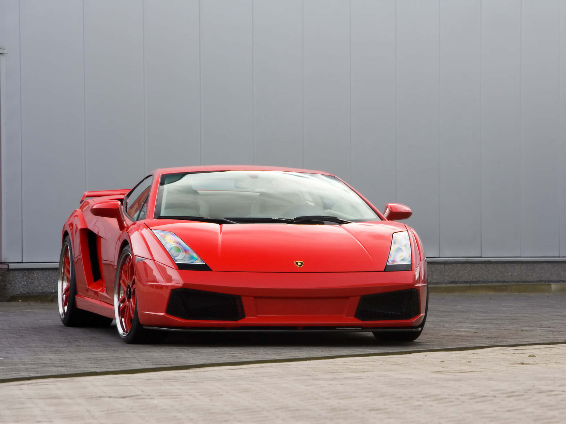 Lamborghini Gallardo 桌布 壁紙 — 一輛鮮紅色的藍寶堅尼Gallardo跑車停放在鋪砌路面上，背景是灰色工業牆。