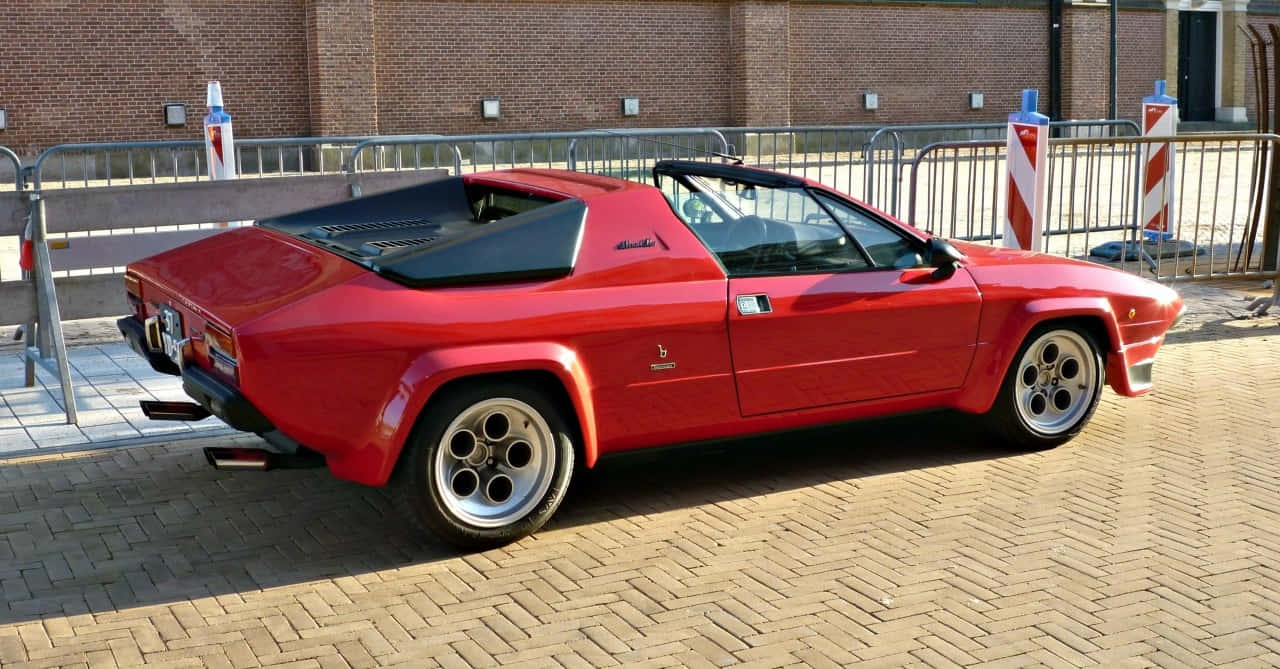 Lamborghini Silhouette 桌布 壁紙 — 一輛鮮紅色的藍寶堅尼Jalpa跑車停在陽光普照的磚砌人行道旁，旁邊有金屬護欄。