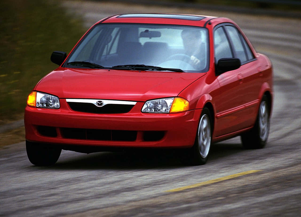Mazda Protege 桌布 壁紙 — 一輛鮮紅色的馬自達轎車在模糊的道路上疾馳，動態模糊強調了其動態移動。